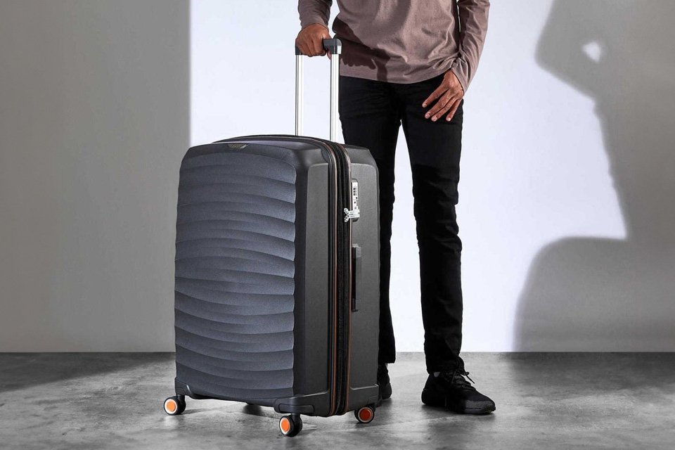 A man with a Rock Expandable 8 wheel Hard large suitcase in charcoal.
